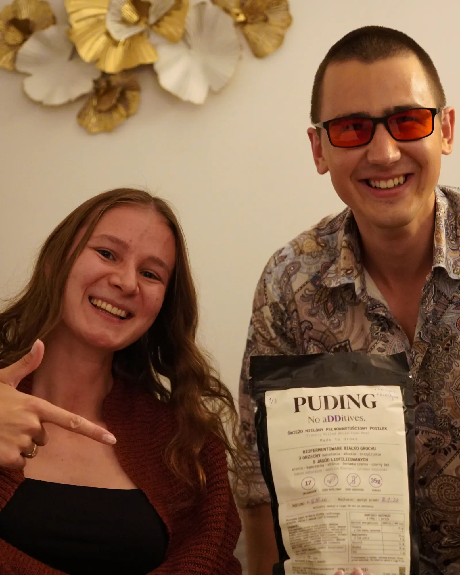 Daria wskazuje paczkę PUDING, którą trzyma Bartosz; oboje uśmiechają się do obiektywu