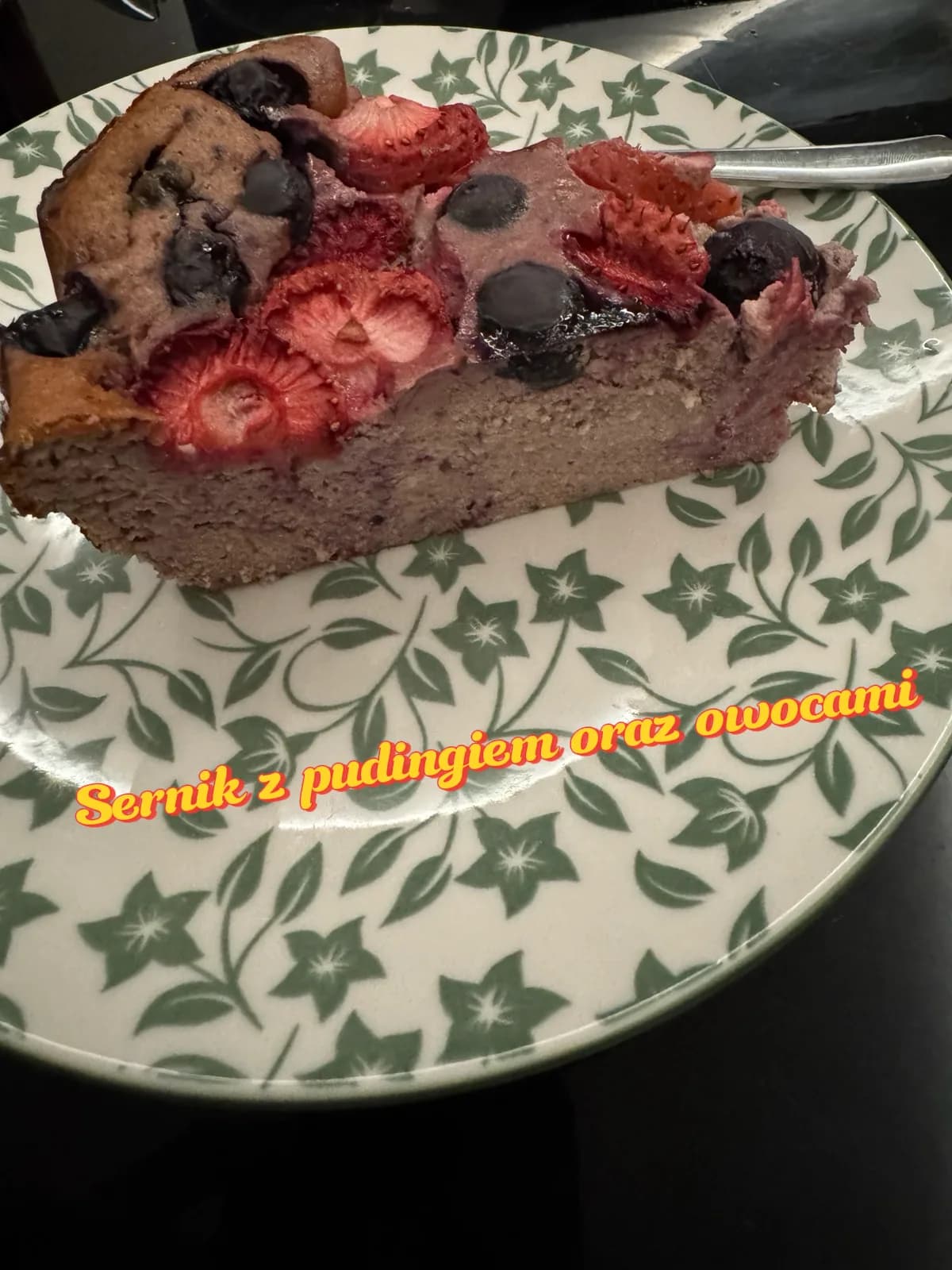 Publiczna relacja na Instagramie: kawałek sernika z pudingiem, truskawkami i borówkami na talerzu